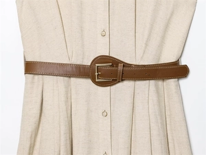 Detail of oat-colored linen dress featuring waist pleats and a brown leather belt with gold buckle