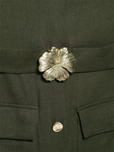Detail of olive green dress featuring a gold floral buckle and metal button accents