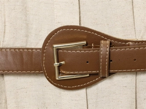 Detail of brown faux leather belt with white stitching and gold metal buckle on dress