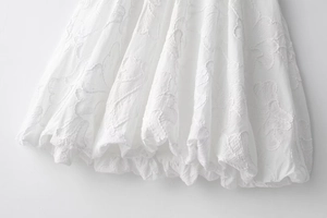 Detailed macro view of white embroidered leaf patterns and pleated hem on a mini dress