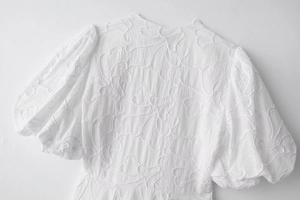 Detail of white summer dress featuring intricate 3D floral embroidery and puffy sleeves