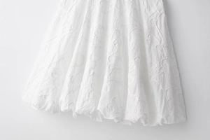 Close-up of white dress showing intricate floral embroidery and pleated 3D fabric textures