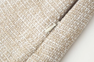 Dettaglio macro del tessuto tweed beige con fili dorati e cerniera invisibile piatta