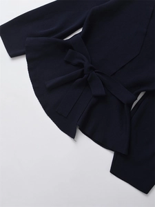 Detail of navy knit top featuring elegant waist bow tie and ruffled hemline texture