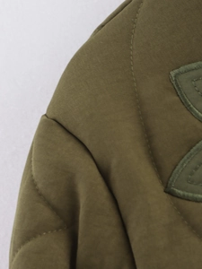 Vue macro du tissu matelassé vert olive avec broderie détaillée sur la veste rembourrée