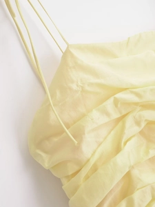 Detail of light yellow summer dress showing fine spaghetti straps and pleated fabric texture