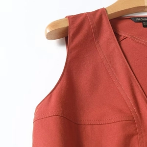 Detail of V-neck sleeveless dress in rust red with twill texture and fine stitching