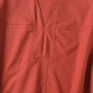 Close-up detail of V-neckline with decorative stitching on brick red sleeveless dress