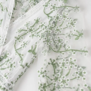Détail du tissu en maille blanche avec broderie florale verte et finitions en dentelle