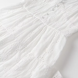 Detailed view of white eyelet embroidery and fabric buttons on V-neck tiered cotton dress