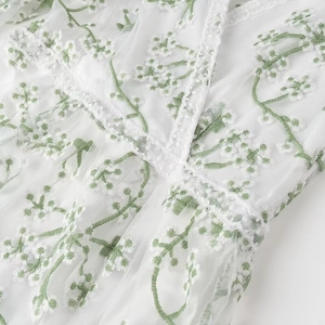 Détail d'une robe en tulle blanc avec broderie florale verte et dentelle au col en V