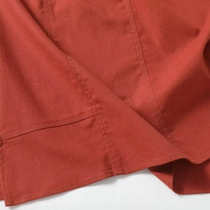Macro detail of burnt orange dress hem showing precision stitching and fabric texture
