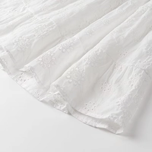 Close-up of white summer dress featuring intricate floral embroidery and layered hem detail