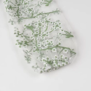 Détail de la manche en tulle blanc avec broderie florale verte et poignet élastique