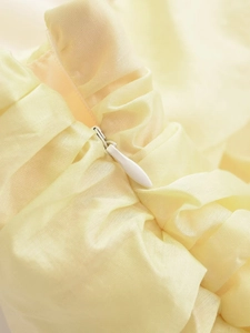 Detailed macro view of the invisible zipper and pleated texture on the light yellow dress