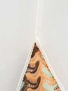 Macro detail of multicolored crochet knit fabric with intricate hollow-out V-neck pattern