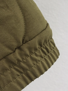 Détail macro des poignets surpiqués de la veste matelassée vert olive à coutures renforcées