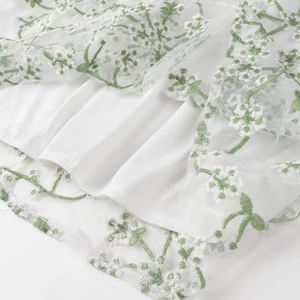 Détail de l'ourlet de la robe blanche avec broderie de fleurs blanches et lierre