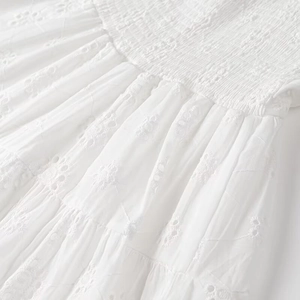 Close-up of white dress showing intricate eyelet embroidery and smocked elastic details