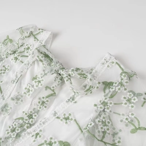 Détail de la broderie florale et du nœud à l'encolure sur une robe blanche et verte