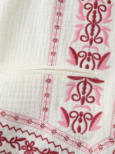 Detail of white textured fabric with ethnic floral embroidery and fine pocket seam