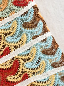 Detail of colorful crochet knit fabric with vibrant wave patterns and white stitching