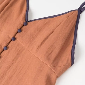 Detailed view of the V-neckline with purple piping and fabric-covered buttons in caramel