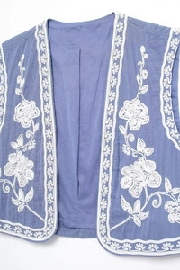 Détail de broderie florale sur un gilet vintage bleu sans manches à bords ondulés