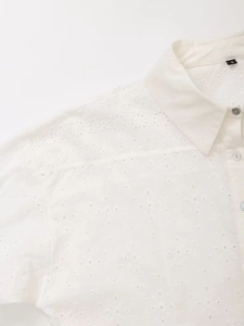 Detail view of French eyelet embroidery on a white long-sleeved shirt with a pointed collar