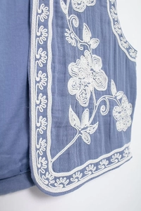 Détail de la broderie florale blanche sur un gilet en coton bleu clair et texture du tissu