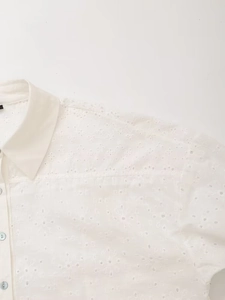 Close-up of white lapel shirt featuring intricate eyelet floral embroidery and blue buttons