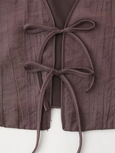 Detail of coffee brown pleated top featuring double tie-up bows and a deep V-neckline