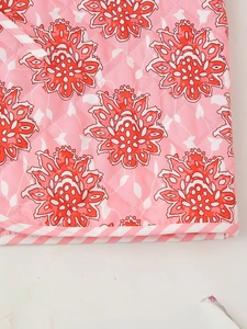 Detailed view of pink floral quilted fabric with mandala patterns and striped piping