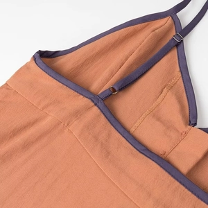 Detail of adjustable spaghetti strap with purple piping on textured orange dress fabric