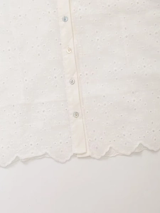 Detail of scalloped hem and pearl buttons on white hollow floral embroidery shirt