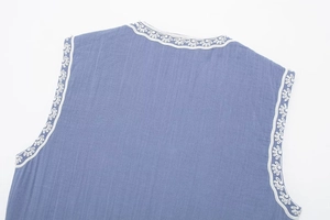 Détail du gilet bleu en coton et lin avec broderie florale blanche sur les bords