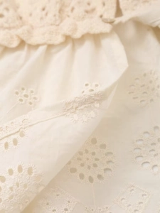 Detailed close-up of cream white crochet lace and eyelet embroidery on a French V-neck top