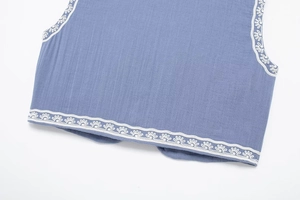 Gros plan détaillé du gilet en lin bleu avec broderie florale blanche sur les bords
