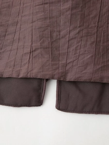 Detail showing the brown pleated fabric texture and split hem of the two-piece set