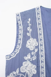 Détail de broderie florale blanche sur un gilet sans manches bleu rétro pour femme