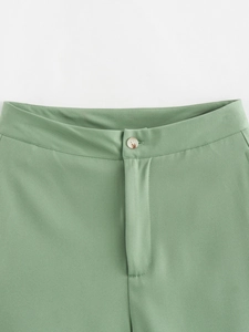 Détail du short vert montrant le tissu en sergé texturé et la fermeture à bouton en résine