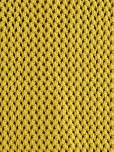 Dettaglio del gilet in maglia gialla con trama a nido d'ape e maglia grossa