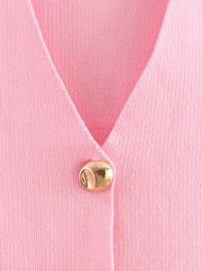 Detail der rosa Strickweste mit V-Ausschnitt und dekorativem unregelmäßigem Goldknopf
