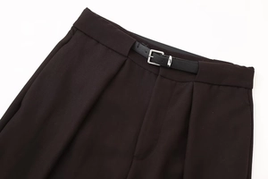 Detail of high-waist trousers with elegant pleats and a slim black leather belt