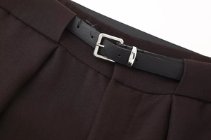 Detail of dark brown trousers waist with textured black leather belt and silver buckle