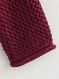 Macro detail of wine red chunky knit fabric with textured honeycomb pattern and rolled edge