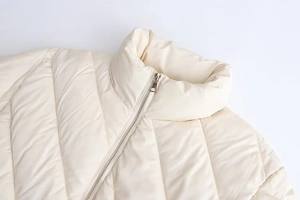 Close-up of cream quilted jacket with stand collar and silver metal zipper detail