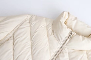 Detailed close-up of stand-up collar and diagonal quilting on cream winter jacket