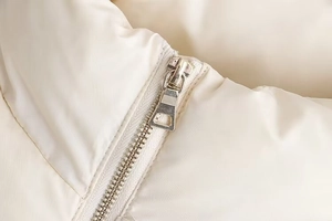 Detailed macro view of the silver metal zipper on an off-white quilted jacket