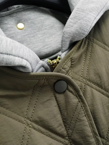 Detailed shot of olive green diamond quilted jacket featuring a grey jersey hood and zipper